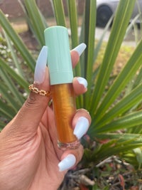 a hand holding a bottle of lip balm in front of a plant