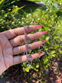 a woman's hand holding a bracelet with emeralds on it