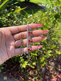 a person's hand holding a pair of cherry bracelets