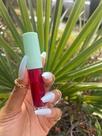 a hand holding a lipstick in front of a palm tree