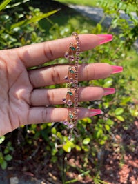 a woman's hand holding a pink and green necklace